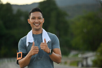 Handsome athletic man running in park and showing thumbs up. Sport and healthy life concept.