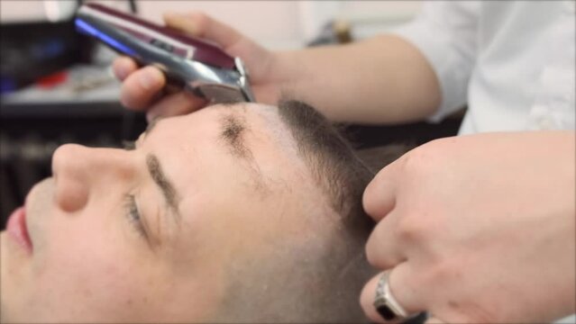 A barber stylist cuts hair from the forehead with a clipper for a male client. Close-up