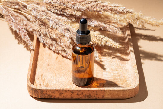 From above amber glass bottle with dropper on wooden tray against a beige background with pampas grass