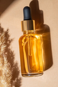 From above luxurious amber glass dropper bottle with golden cap, standing next to soft pampas grass on a warm backdrop