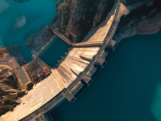 Top view of a massive dam structure with a reservoir in the mountains during clear weather