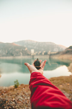 Anonymous hand holding a compass with a scenic lake and mountains in the background symbolizing guidance and exploration