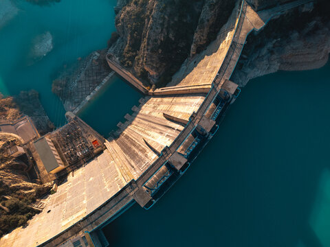 Top view of a massive dam structure with a reservoir in the mountains during clear weather