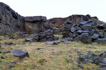 A small disused stone quarry with large wet boulders, and rocks piled around. The rock face of the quarry can be seen in the background.