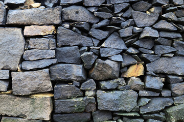 Wall of dark weathered stones with spots of lichen. 