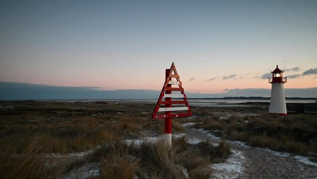 Footage of lighthouse List West and red-white triangular, wooden directional signs (border beacon) serving as day markers at evening in winter landscape.Sylt, Lighthouse Ellenbogen, Northernmost point