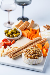 Cheese platter with persimmons, olives and wine on white marble board for party.
