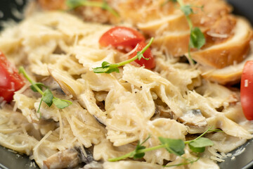 Farfalle with chicken breast and parmesan in cream sauce in a black plate on the kitchen table, close-up. Traditional Italian pasta
