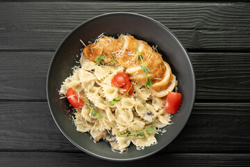 Tasty appetizing classic italian farfalle pasta with chicken breast, cheese parmesan on black plate on dark wooden table. View from above