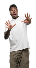 Young african american man wearing white t-shirt afraid and terrified with fear expression stop gesture with hands, shouting in shock. Panic concept.