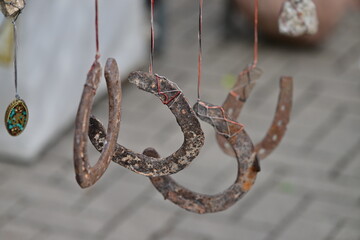 Four rusty horseshoes hanging on thin ropes in front of a blurred, gray background.