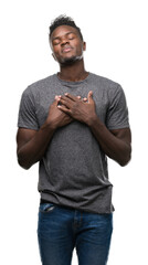 Young african american man wearing grey t-shirt smiling with hands on chest with closed eyes and grateful gesture on face. Health concept.