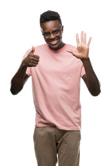 Young african american man wearing pink t-shirt showing and pointing up with fingers number six while smiling confident and happy.
