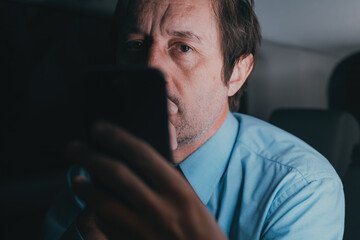 Businessman using cell phone at the back seat of the car will traveling home from the work late at night, low key
