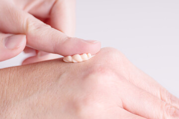 Naklejka premium Female hands care. Close up of woman applying cream on hand skin. Skin care cosmetics in peach fuzz color