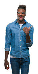 Fototapeta premium Young african american man over isolated background smiling with happy face looking and pointing to the side with thumb up.