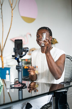 Black man in a white sweater enthusiastically demonstrates skincare products in front of a camera setup
