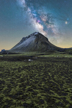 A solitary snow-capped mountain under a clear night sky illuminated by the Milky Way in Iceland winter landscape