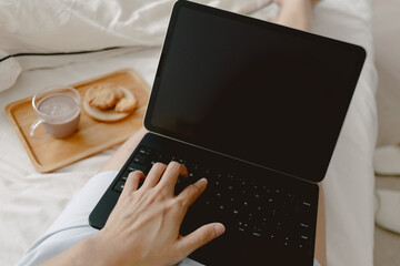 Woman hand tying keyboard laptop, showing black screen display putting on lap, working at home while eating cookie and coffee on white bed at home, lifestyle freelance concept.