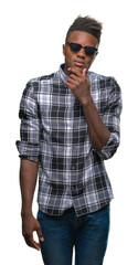 Young african american man wearing sunglasses over isolated background with hand on chin thinking about question, pensive expression. Smiling with thoughtful face. Doubt concept.