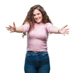 Beautiful brunette curly hair young girl wearing pink sweater over isolated background looking at the camera smiling with open arms for hug. Cheerful expression embracing happiness.