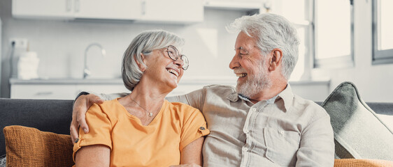 Happy laughing older married couple talking, laughing, standing in home interior together, hugging...
