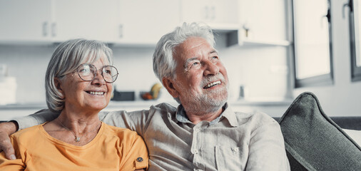 Obraz premium Dreamy middle aged senior loving retired family couple looking in distance, planning common future or recollecting memories, enjoying peaceful moment relaxing together on cozy sofa in living room.