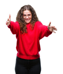 Beautiful brunette curly hair young girl wearing glasses and winter sweater over isolated background looking at the camera smiling with open arms for hug. Cheerful expression embracing happiness.