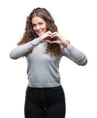 Beautiful brunette curly hair young girl wearing a sweater over isolated background smiling in love showing heart symbol and shape with hands. Romantic concept.