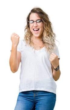 Beautiful young blonde woman wearing glasses over isolated background very happy and excited doing winner gesture with arms raised, smiling and screaming for success. Celebration concept.