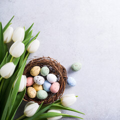 Beautiful white tulips with colorful quail eggs in nest on light gray stone background. Spring and...