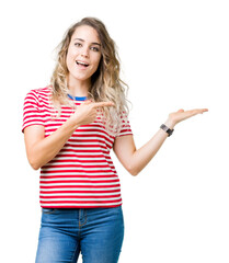 Beautiful young blonde woman over isolated background amazed and smiling to the camera while presenting with hand and pointing with finger.