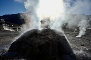 Steam rising from a bolder geyser at The Geysers Del Tatio, Antofagasta, Chile, with blue skies behind. 