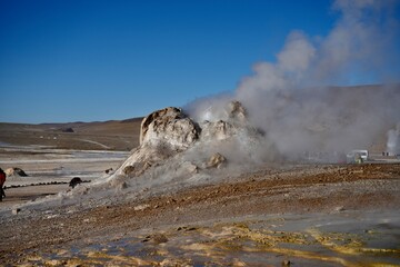 Steam rising from the ground with hills and blue skies behind, at Geysers Del Tatio, Antofagasta, Chile.