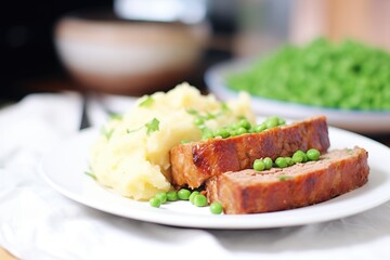 sliced meatloaf on a plate with green peas and mashed potatoes
