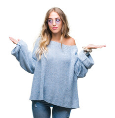 Beautiful young blonde woman wearing sunglasses over isolated background clueless and confused expression with arms and hands raised. Doubt concept.