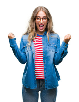 Beautiful young blonde woman wearing glasses over isolated background celebrating surprised and amazed for success with arms raised and open eyes. Winner concept.