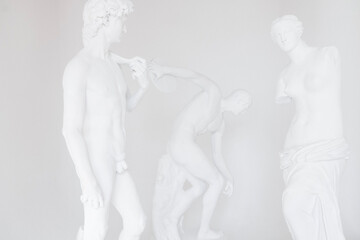 Group of plaster statues on white backdrope. Bonded marble sculptures of Discus thrower, David and Venus.
