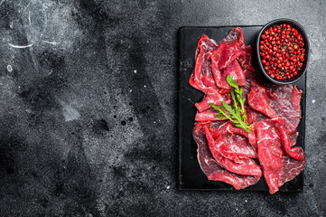 Slices of Beef Capriccio, raw marbled meat. Black background. Top view. Copy space
