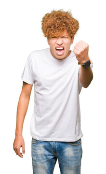 Young handsome man with afro hair wearing casual white t-shirt angry and mad raising fist frustrated and furious while shouting with anger. Rage and aggressive concept.