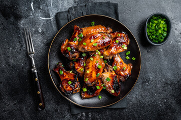 Baked chicken wings with sweet chili sauce in a plate. Black background. Top view