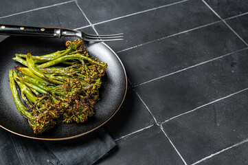 Roasted green Broccolini Sprouts with garlic butter in a plate. Black background. Top view. Copy...
