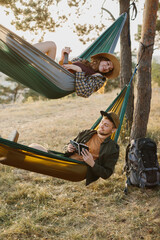 A guy and a girl are relaxing in hammocks in a pine forest at sunset.