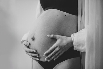 Closeup belly of a woman. Pregnancy motherhood procreation concept. Pregnant female waiting for newborn baby. Young girl touching and holding belly, caring about health indoors. Black and white photo - obrazy, fototapety, plakaty