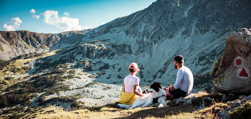 couple with dog sitting on rocks admiring mountain landscape slow travel