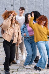 Casual, cheerful friends enjoy dancing together on a paved area, with expressions of happiness and...