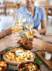 Friends with white wine toasting over served table with food