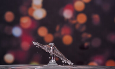 Drop of water falling and colliding forming a tilted water hat with a dark background of defocused...