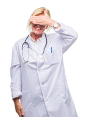 Middle age blonde doctor woman over isolated background smiling and laughing with hand on face covering eyes for surprise. Blind concept.