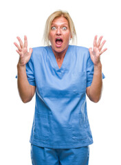 Middle age blonde woman wearing doctor nurse uniform over isolated background crazy and mad shouting and yelling with aggressive expression and arms raised. Frustration concept.